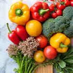 Alimentos frescos y coloridos como verduras, frutas y granos integrales dispuestos artísticamente sobre una tabla de madera, evocando nutrición y salud.